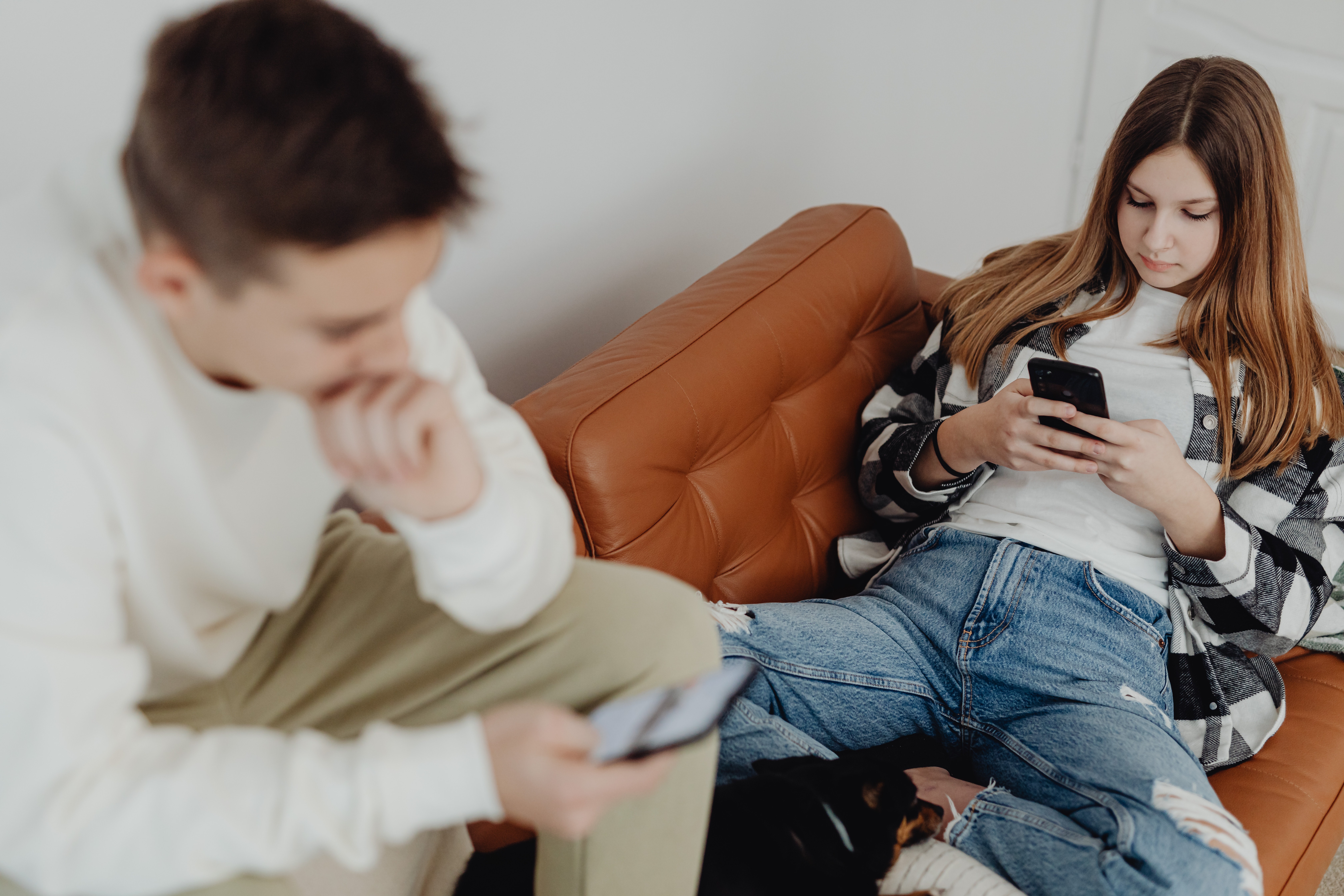 Girl sitting on sofa playing on her phone, boy sitting next to her